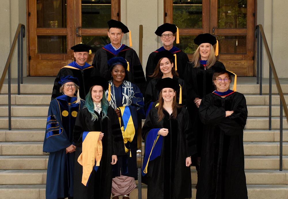 4 graduates surrounded by 6 faculty, all wearing graduation regalia.