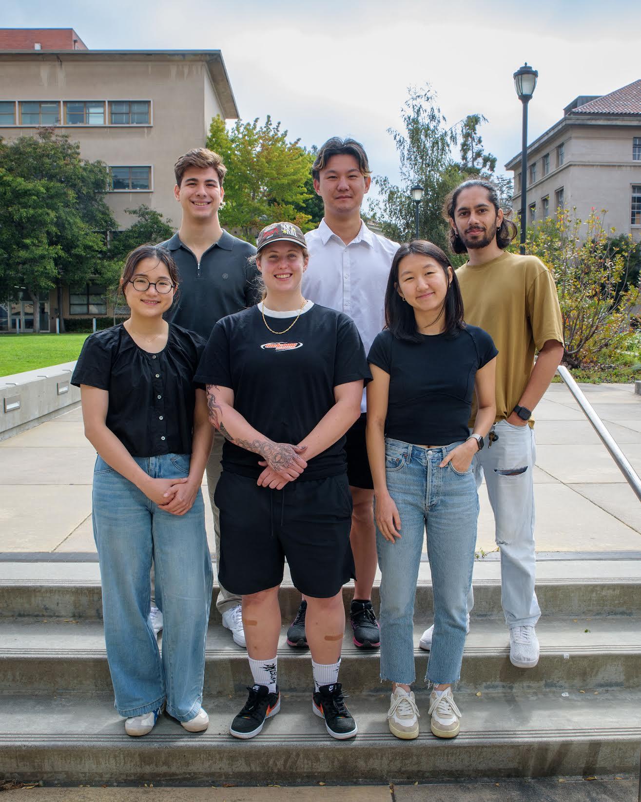  6 people standing outside on steps on campus, smiling