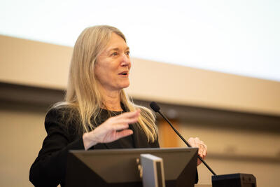 Cori Bargmann giving a talk in front of a microphone, smiling and gesturing with her hands.